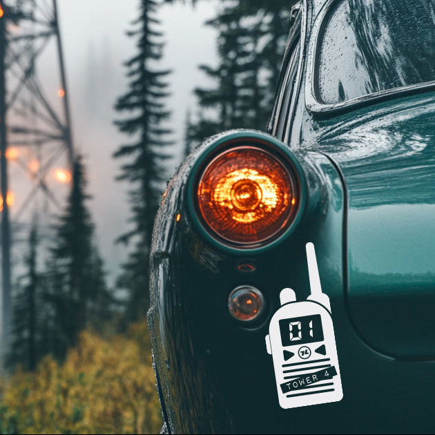 Car with a walkie-talkie sticker in front of a fire tower and trees