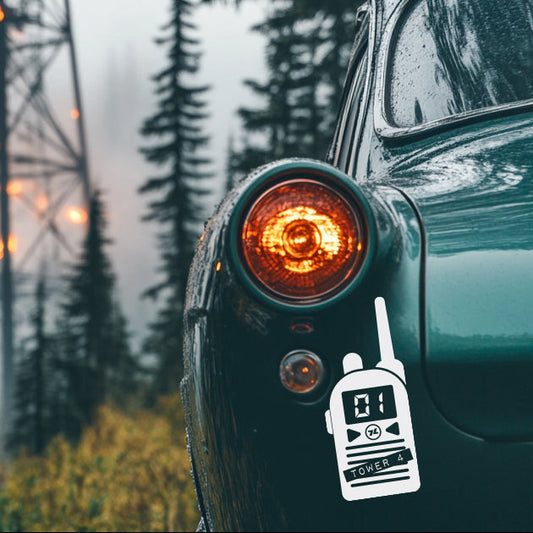 Car with a walkie-talkie sticker in front of a fire tower and trees